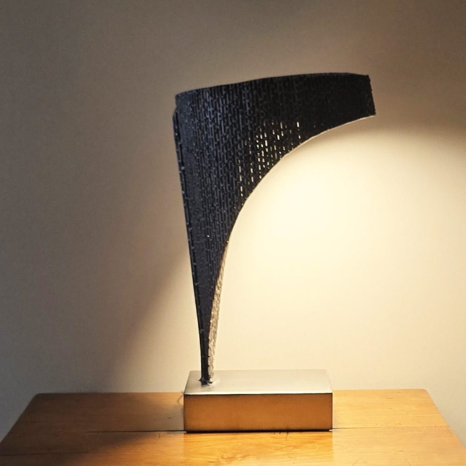 Sype 017 – Vue latérale lumineuse Œuvre Sype 017 Luminaire tissé, lumière chaude révélant les soudures et textures de l’acier brut.