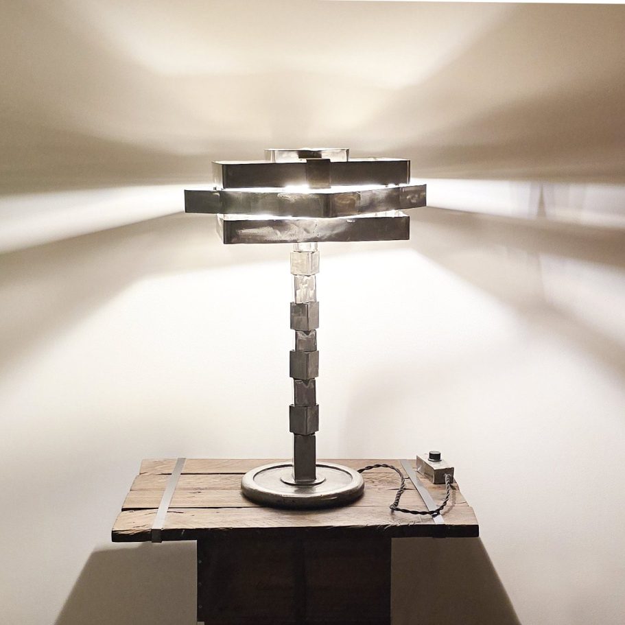 Lampe Sype 003 en acier brut, sculpture lumineuse équilibrée sur pied circulaire