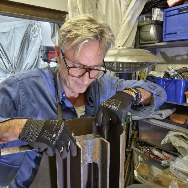 Vie d’atelier – Sype à l’œuvre, façonnant la lumière dans l’acier. Sype en train de souder une lampe en acier brut dans son atelier – travail artisanal et précision du geste.