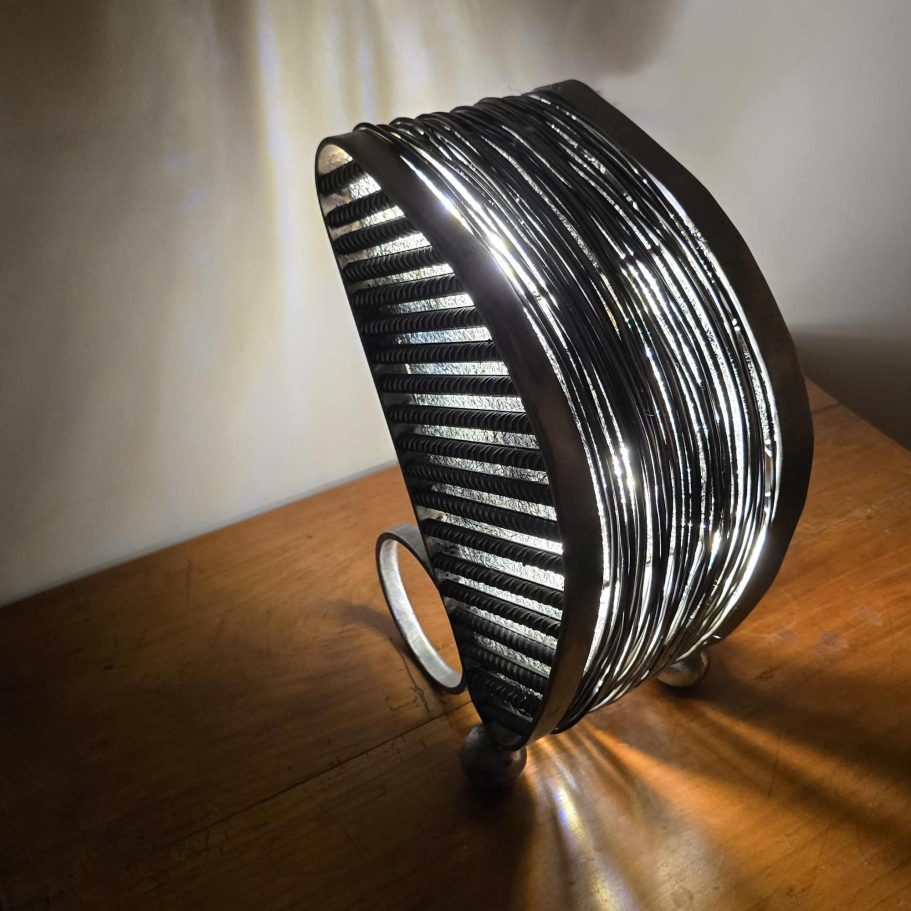 Détail latéral de la sculpture Sype 014 Dualité Métallique, anneaux d’acier et texture du béton révélés par la lumière.