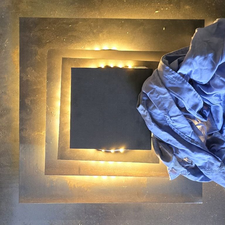 Détail d’une œuvre lumineuse en acier signée Sype Design — lumière chaude, matière brute et empreinte du geste artisanal.