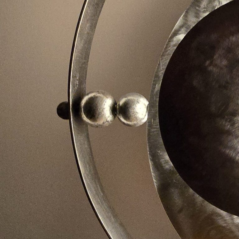 Détail latéral de la lampe Éclipse Sonore Sype 015, anneaux et sphères d’acier jouant avec les reflets de la lumière.