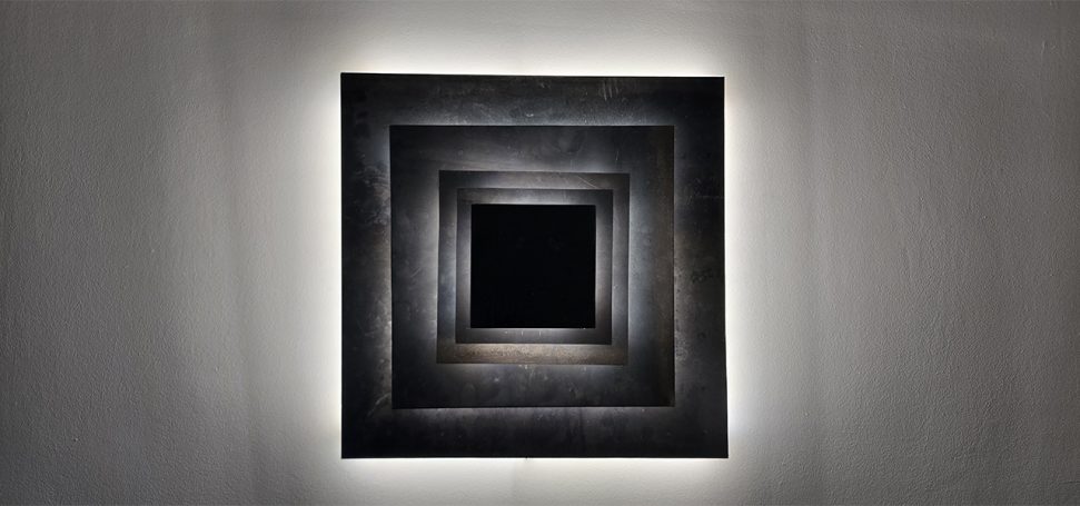 Sype 010 – Pyramide de carrés – Applique murale en acier brut Applique murale en acier brut composée de carrés superposés avec éclairage LED indirect.