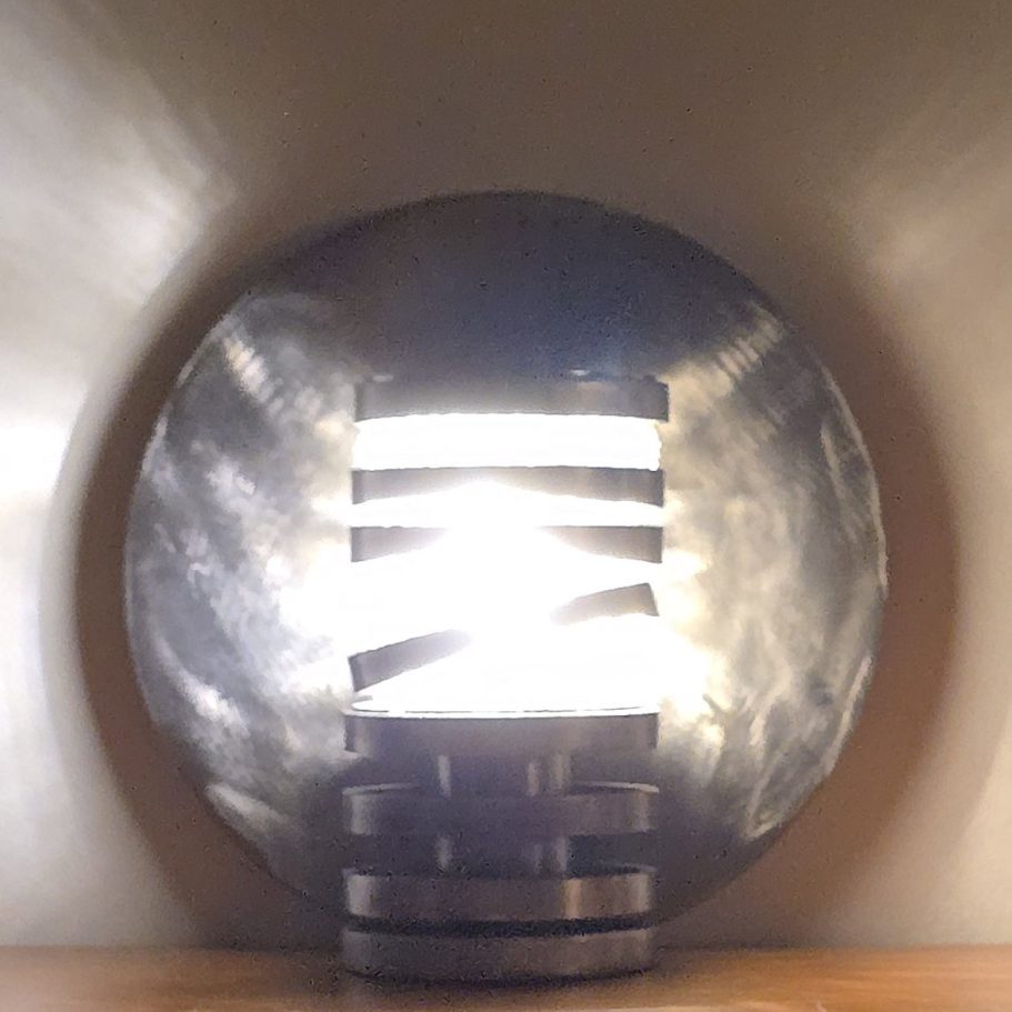 Spirale d’acier Sype 006, lampe contemporaine en acier projetant des reflets lumineux sur le mur.