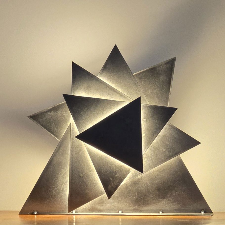 Œuvre Sype 016 Danse des Angles, lampe-sculpture triangulaire projetant une lumière diffuse et graphique.