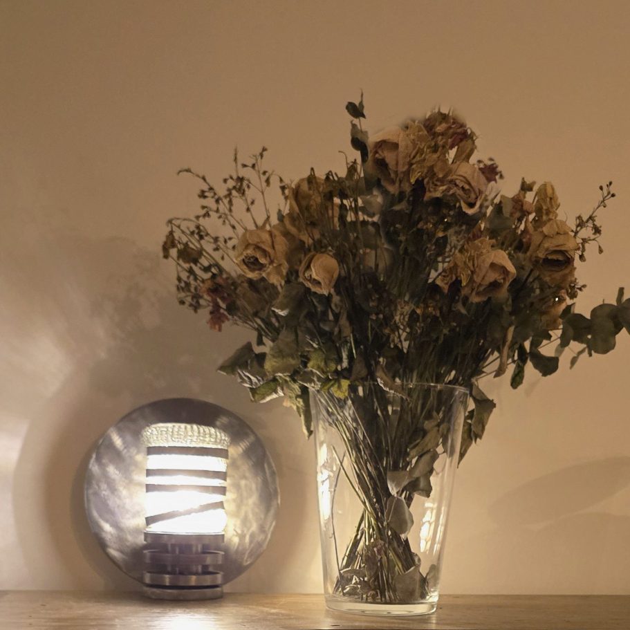 Lampe Spirale d’acier Sype 006 posée près d’un bouquet, alliance entre design brut et poésie lumineuse.