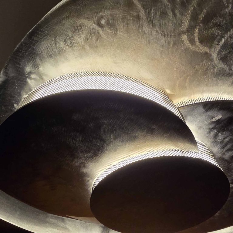 Détail de la sculpture Éclipse Sonore montrant l’empilement de disques en acier et la lumière intégrée révélant les volumes.